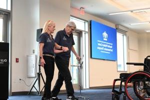 A man walking assisted by a woman and a cane